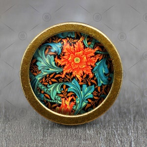 Puede incluir: Un pomo redondo de latón con un diseño floral. El pomo presenta un patrón repetitivo de flores naranjas y hojas verde azuladas sobre un fondo negro.