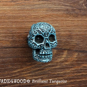 Może przedstawiać: Turkusowy, czaszkowaty gałka do szafki z misternymi wzorami kwiatowymi. Gałka jest wykonana z metalu i ma błyszczące wykończenie.