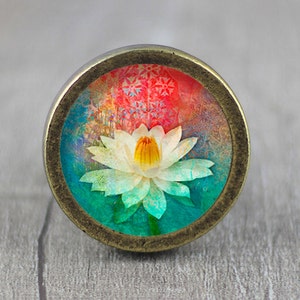 May include: A round, brass-coloured knob featuring a colourful image of a white lotus flower with a yellow centre. The background is a vibrant mix of red, blue, and green.