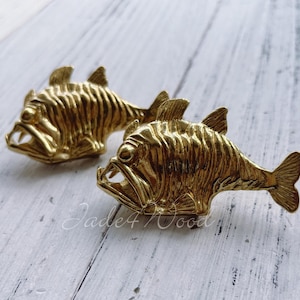 May include: Two gold-coloured fish sculptures with detailed scales and open mouths. The fish are facing different directions and have a realistic appearance.