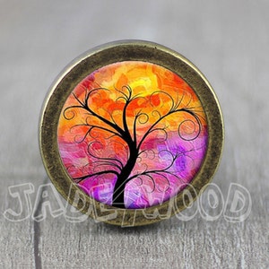 May include: A round, bronze-colored knob with a colorful, abstract tree design. The tree is painted in shades of pink, orange, and yellow, with black branches and swirls.