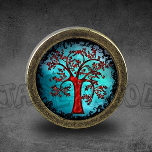 Puede incluir: Un colgante redondo de color bronce con un diseño de árbol estilizado. El árbol tiene un tronco y ramas rojas con hojas rojas, sobre un fondo turquesa. El colgante tiene un borde oscuro y un fondo gris.