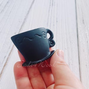 May include: A black ceramic teacup with a decorative swirl design. The teacup is held in a hand.