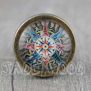 May include: A round, brass-colored knob with a glass insert featuring a colorful compass rose design. The compass rose has a red, blue, and white color scheme.
