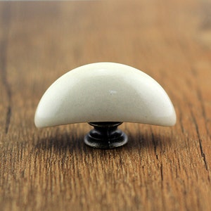 Op de afbeelding: Witte keramische kastknop met een halfronde vorm en een bronzen basis.