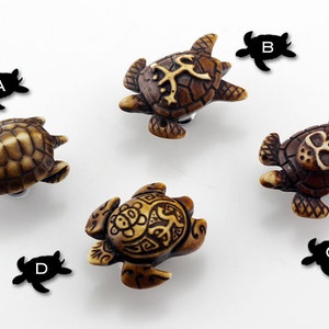 Może przedstawiać: Cztery ozdobne figurki żółwi z misternymi rzeźbami. Każdy żółw ma unikalny wzór, w tym czaszkę, krzyż i wzory geometryczne. Żółwie są wykonane z brązowego materiału i mają realistyczny wygląd.