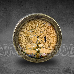 May include: A round, gold-toned metal knob with a glass insert featuring a painting of a tree with swirling branches in shades of gold and brown. The tree is set against a light beige background.