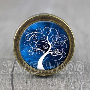Puede incluir: Un pomo redondo de color latón con un diseño de árbol de la vida azul y blanco. El árbol es blanco con un patrón de espiral y puntos.