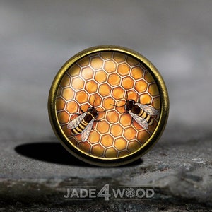 May include: A gold-toned round button with a honeycomb pattern and two bees. The bees are black and yellow with brown wings.