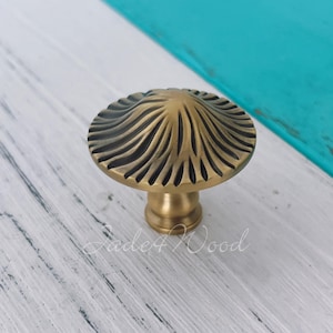 May include: A brass cabinet knob with a ridged, mushroom-shaped design. The knob is set against a white and turquoise painted wooden surface. The text "Jade4Wood" is visible. The knob is suitable for furniture.