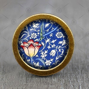May include: A round, gold-colored knob with a blue and white floral design featuring a red and white tulip. The knob has a raised, circular rim.