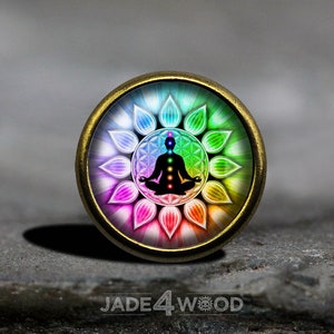 Peut inclure: Un pendentif rond de couleur laiton avec une image colorée d'une figure méditant avec sept chakras. La figure est entourée d'un motif floral aux couleurs arc-en-ciel.