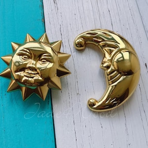 Può includere: Decorazione da parete in metallo dorato a forma di sole e luna. Il sole ha un viso sorridente e la luna è a forma di mezzaluna.