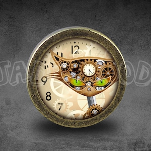 May include: A round, brass-colored clock face with a cat design. The cat's eyes are green and the clock face is surrounded by gears. The clock face has Roman numerals and a smaller clock face in the center.