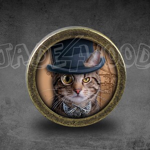 Może przedstawiać: Okrągły guzik w kolorze mosiądzu z kotem w cylindrze i monoklem. Kot patrzy bezpośrednio na widza. Tło to rysunek w stylu vintage przedstawiający statek.