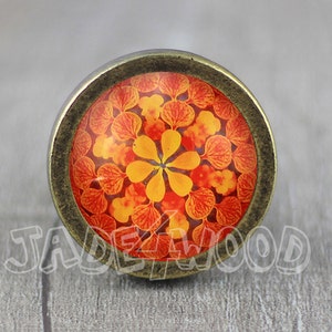 May include: A round, bronze-colored knob with a glass insert featuring a red and orange floral design.