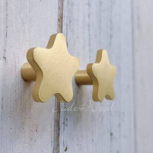 Op de afbeelding: Twee gouden stervormige kastknoppen. De grotere knop bevindt zich links en de kleinere knop rechts.