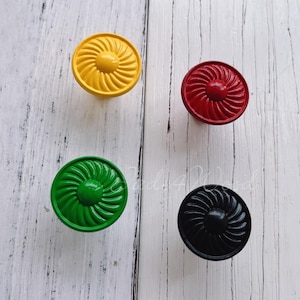 Könnte beinhalten: Vier dekorative Schrankknöpfe mit einem Wirbelmuster. Die Knöpfe sind gelb, rot, grün und schwarz.