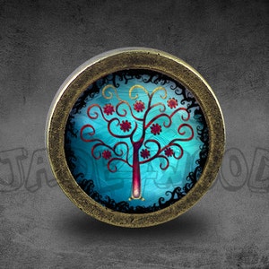 Puede incluir: Un pomo decorativo redondo de color latón con un inserto de vidrio que presenta un árbol estilizado con flores rojas y remolinos azules y dorados sobre un fondo azul.
