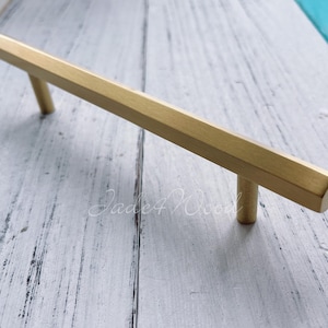 Pode incluir: Uma puxador de armário hexagonal de cor dourada com acabamento escovado. O puxador mede aproximadamente 10 cm de comprimento.