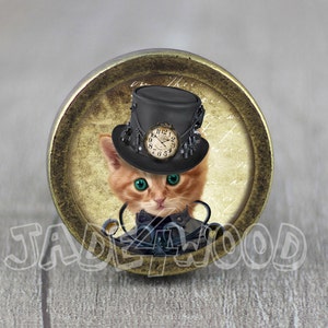 May include: A round, gold-colored knob with a vintage-style image of a cat wearing a top hat with a clock face. The cat has green eyes and a black bow tie.