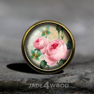 Peut inclure: Un bouton rond en métal doré avec un cabochon en verre représentant un motif floral vintage. Le motif comprend des roses roses et des papillons verts sur un fond crème.
