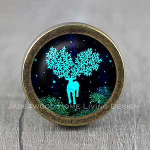 以下が含まれることがあります： 鹿の角から木が生えている青い緑色の鹿の画像が描かれた、真鍮色の丸いノブ。背景は濃い青色で白い星が散りばめられています。