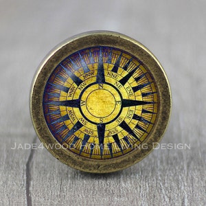 May include: A gold-colored compass knob with a black compass rose and blue and red accents. The compass rose has the cardinal directions and intermediate directions labeled.