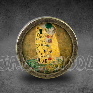 Könnte beinhalten: Ein runder, messingfarbener Knopf mit einem Glaseinsatz, der eine Reproduktion von Gustav Klimts Gemälde "Der Kuss" zeigt. Das Gemälde zeigt zwei Figuren in einer leidenschaftlichen Umarmung vor einem goldenen und gelben Hintergrund.