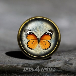 May include: A round, gold-toned metal button with a glass top featuring a vintage-style image of an orange and black butterfly on a blue and white patterned background.