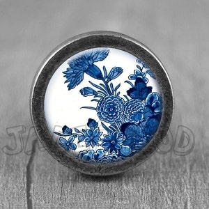 May include: A round, silver-toned knob with a blue and white floral design. The knob features a white background with blue flowers and leaves.