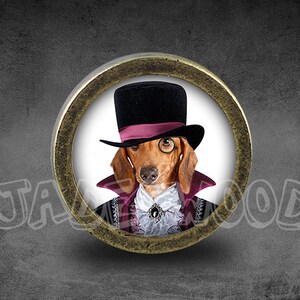 Peut inclure: Un teckel portant un haut-de-forme noir avec un ruban rose, un monocle et un collier en velours violet. Le chien regarde directement la caméra. L'image est dans un cadre circulaire avec une bordure dorée.