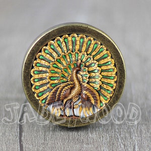 May include: A round, brass-colored knob with a peacock design. The peacock has a green and gold tail with a brown body.