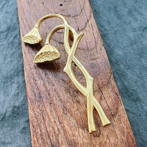 Op de afbeelding: Gouden metalen deurknop met een bloemmotief. De knop is gevormd als twee gestileerde bloemen met stelen.