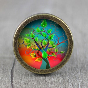 May include: A round, bronze-colored cabinet knob with a colorful image of a stylized tree with green leaves and a red, orange, and blue background.