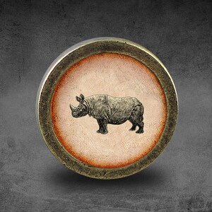 May include: A round, bronze-colored, decorative knob with a raised, circular design. The center of the knob features a black and white image of a rhinoceros.