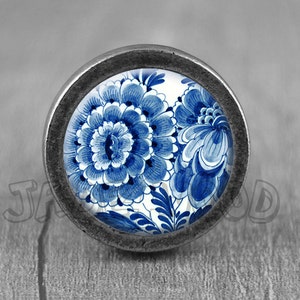 May include: A blue and white floral design on a round knob with a silver metal frame.