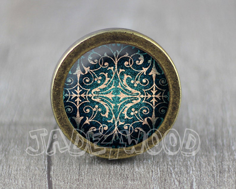 May include: A round, brass-coloured cabinet knob with a teal and gold patterned design.