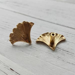 Może przedstawiać: Dwa złote, gładkie gałki meblowe w kształcie liścia miłorzębu. Gałki mają szczegółowy wzór i gładkie, polerowane wykończenie.