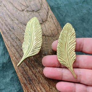 May include: Two gold-colored metal feather-shaped drawer pulls. The pulls have a detailed, textured design.