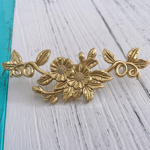 May include: Gold-toned metal floral design with two large flowers and leaves. The design is intricate and detailed, with a vintage style.