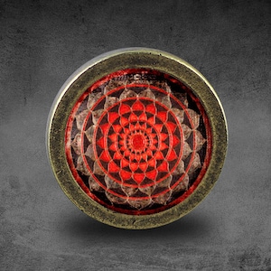 Può includere: Un ciondolo rotondo color ottone con un design a mandala rosso e marrone. Il mandala presenta intricati motivi geometrici e un cerchio centrale.