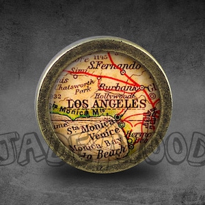 Op de afbeelding: Een ronde, messingkleurige, decoratieve kaart van Los Angeles, Californië. De kaart is in vintage stijl en toont de namen van wijken en bezienswaardigheden, waaronder Santa Monica, Venice, Hollywood en Burbank.