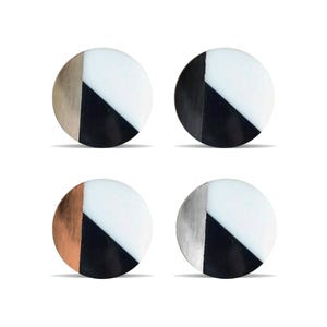 May include: Four circular stud earrings with a geometric design. Each earring has a section of white, black, and a metallic colour: gold, black, copper, and silver. The earrings are shown against a white background.