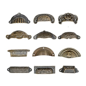 Peut inclure: Une collection de poignées de tiroir anciennes de formes et de motifs variés. Les poignées sont en métal avec une finition bronze vieilli. Certaines présentent des motifs ornés, d'autres ont un design incurvé plus simple. Une poignée porte l'inscription "THE GEM PAINTING SHOP PORTBELLO RD LONDON".