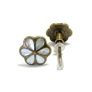 May include: Two flower-shaped earrings with a vintage brass finish. Each earring features a mother-of-pearl inlay in a five-petal design. One earring is fully assembled with a post and backing, while the other is partially disassembled.