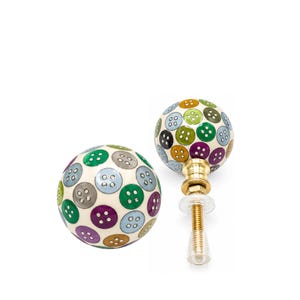 May include: Two round ceramic cabinet knobs featuring a cream-colored base decorated with a repeating pattern of small, colorful buttons in shades of green, blue, purple, grey, and gold. Each knob includes a brass-toned metal bolt and hardware.