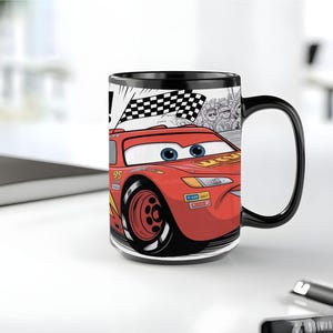 K&ouml;nnte beinhalten: Ein schwarzer Keramikbecher mit einer grafischen Illustration eines roten Rennwagens mit der Nummer 95 an der Seite. Das Design zeigt eine Zielflagge, eine Zuschauermenge sowie die blauen Augen und den l&auml;chelnden Mund des Autos.