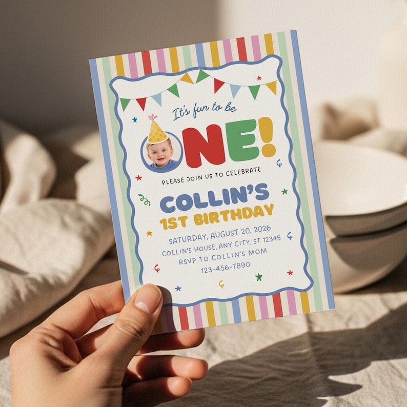May include: A rectangular birthday invitation card featuring a colourful vertical striped border. The text reads: It's fun to be ONE! PLEASE JOIN US TO CELEBRATE COLLIN'S 1ST BIRTHDAY SATURDAY, AUGUST 20, 2026 COLLIN'S HOUSE, ANY CITY, ST 12345 RSVP TO COLLIN'S MOM 123-456-7890.