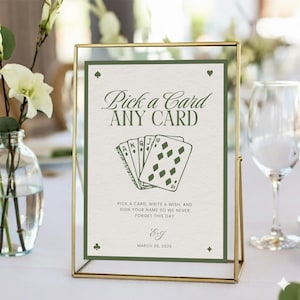 May include: A gold-framed sign with the text "Pick a Card ANY CARD" in elegant script. The sign features a deck of cards illustration and the text "Pick a card, write a wish, and sign your name so we never forget this day."